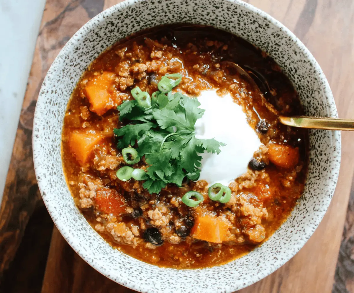 Hearty sweet potato turkey chili in a bowl garnished with fresh herbs and topped with shredded cheese, perfect for a warming meal.